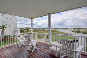 A covered deck with white Adirondack chairs and a view of a river and buildings in the background. - 5BR Ocean View House - Hot Tub - Boat Access (North Topsail Beach)