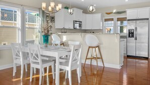 A modern kitchen with white cabinetry, a stainless steel refrigerator, and a dining area with white chairs and a table.