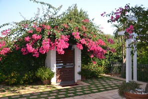Un jardin agrémenté d’une pergola blanche, d’une porte en bois et d’un chemin pavé.