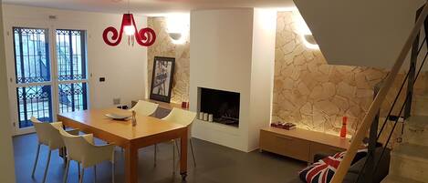 A modern living room with a dining area, a fireplace, and a staircase.