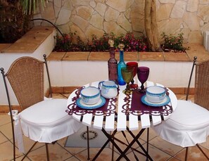 Une table ronde recouverte de nappes blanches, agrémentée de tasses à thé bleues et blanches, d’un vase et de verres colorés.