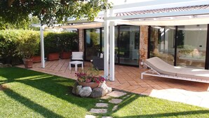 A covered patio area with outdoor seating, a lounge chair, and a potted plant.