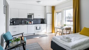A modern hotel room with a bed, a small desk, a chair, a sofa, a kitchen area, and a window with curtains. - Hiisi Homes Kirkkonummi Laajakallio (Kirkkonummi)