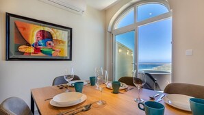 Ein Esstisch mit Tellern, Gläsern und Besteck, ein Bild an der Wand und ein großes Fenster mit Blick.