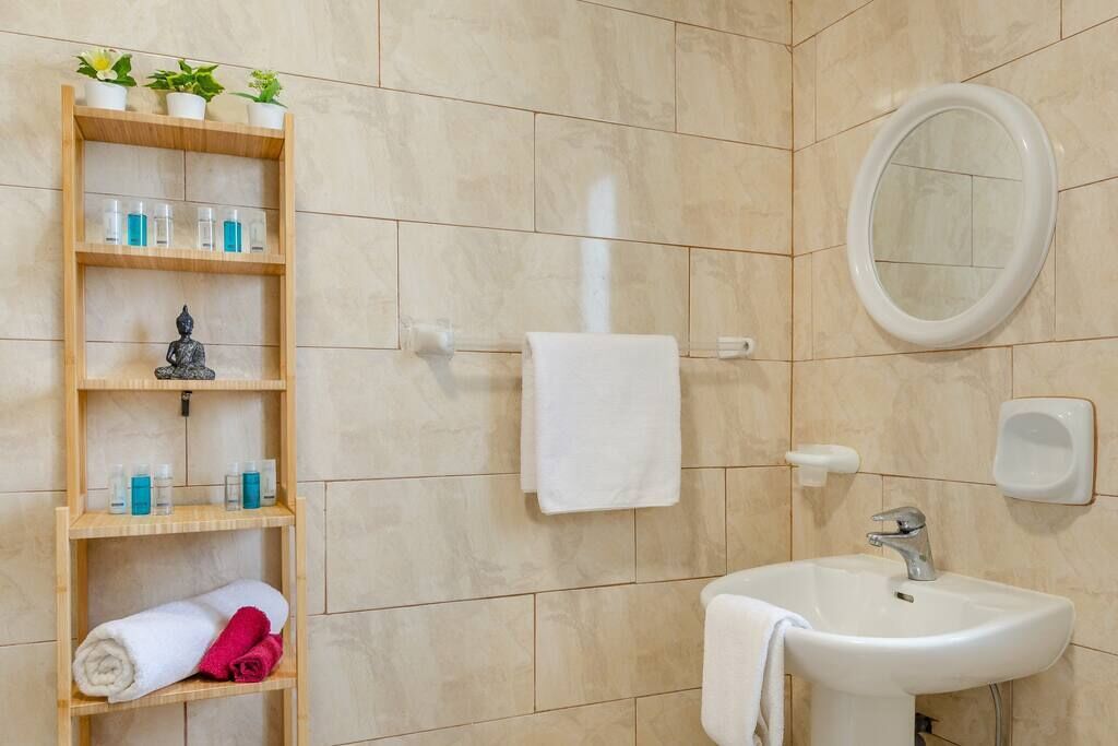Et badeværelse med en hvid vask, et spejl, en håndklædestang og en hylde med toiletartikler.