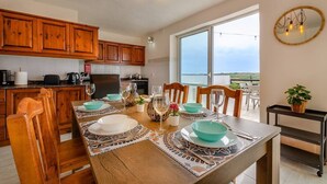 Ett modernt kök med träskåp, ett matbord för fyra personer och ett stort fönster med utsikt över omgivningarna.