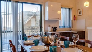 Zona pranzo con tavolo apparecchiato per quattro, cucina sullo sfondo e vista su una scala che conduce all'esterno.