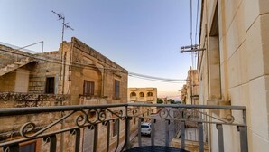 Un balcone con ringhiera in metallo che si affaccia su una strada con edifici e un'auto parcheggiata.