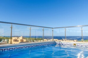 Une piscine à débordement située sur le toit, avec une eau d’un bleu cristallin, entourée de rampes de verre, et offrant une vue sur le paysage environnant.