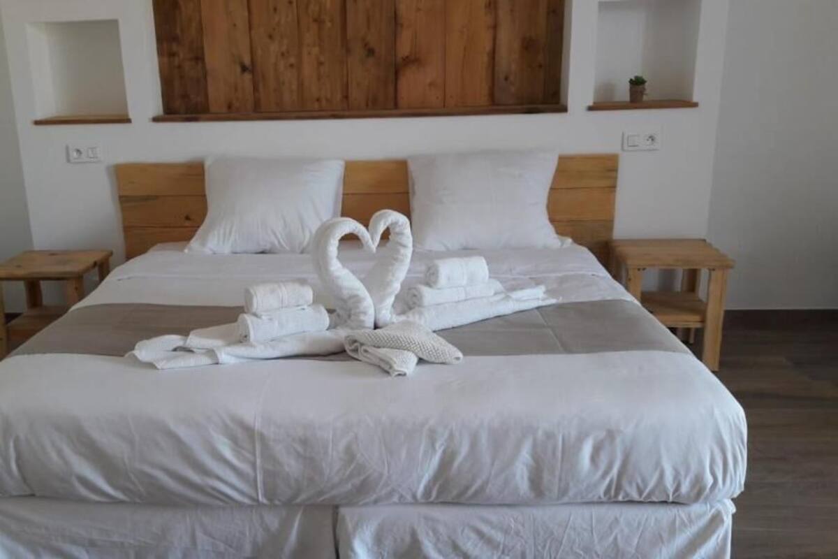 A neatly made bed with white linens and two towels arranged in a heart shape.