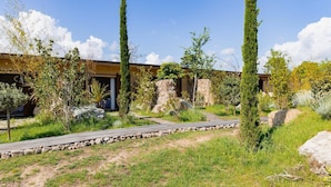 A modern building with a stone facade, surrounded by a landscaped garden with pathways and various shrubs. - Résidence La Plage (Porto-Vecchio)