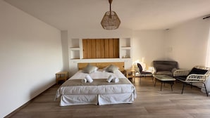 A bedroom with a large bed, two bedside tables, a wooden headboard, a wicker chair, a sofa, and a hanging light fixture. - Résidence La Plage (Porto-Vecchio)