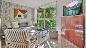 Un salon moderne avec un canapé gris, un fauteuil à rayures et une table basse. Un téléviseur à écran plat est fixé sur un meuble en bois.
