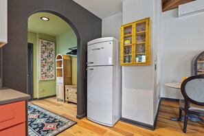 Eine kleine Küche mit einem weißen Kühlschrank, einem Holzkasten und einem gemusterten Teppich.