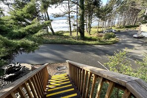A wooden staircase leading to a parking area with a view of the ocean and trees.
