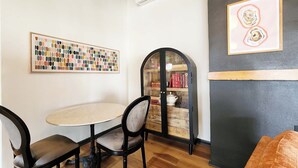 A room with a round table, two chairs, a bookshelf, and two framed artworks. - Ocean Front, The Pink Oyster @ Betty's Beachside, Stairs to the Beach! (Yachats)