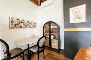 A room with a round table, two chairs, a bookshelf, and two framed artworks. - Ocean Front, The Pink Oyster @ Betty's Beachside, Stairs to the Beach! (Yachats)