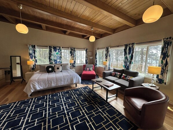 Une chambre à coucher avec un lit, un fauteuil rouge, un canapé gris, une table basse et un tapis à motifs.