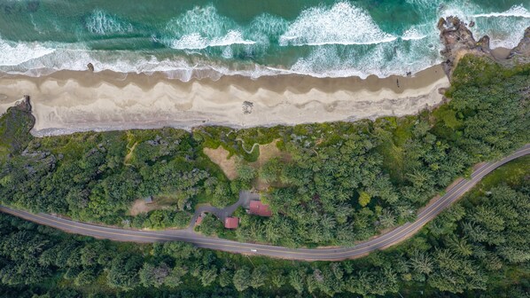 An aerial view of a coastal road with a beach and dense forest.