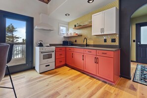 Eine moderne Küche mit Holzboden, weißen und roten Schränken, einem eingebauten Ofen und einem Fenster mit Blick auf einen Wald.