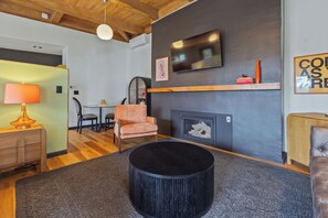 Ein modernes Wohnzimmer mit Kamin, einem darüber montierten Fernseher und einem runden, schwarzen Ottomanen in der Mitte.