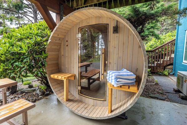 Une structure cylindrique en bois, abritant un banc et une table, et entourée de verdure.