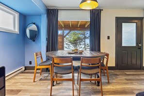 A dining area with a round wooden table, four chairs, a mirror, and a door with a frosted glass panel.