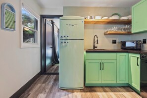 A kitchen with a vintage-style refrigerator, a microwave, and a wooden shelf above the sink.