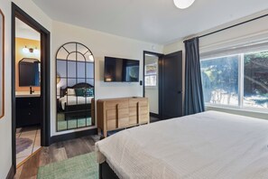 A bedroom with a bed, a dresser, a television, and a large window.