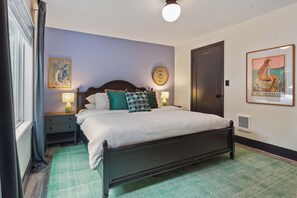 Une chambre à coucher comprenant un lit, deux tables de chevet, une lampe fixée au mur, une porte et deux éléments de décoration murale.