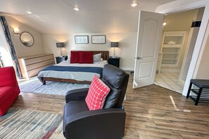 A bedroom with a bed, a red chair, a black leather sofa, and a walk-in closet. - Ocean Front, Agate at Oregon House, Stairs to the Beach! (Yachats)