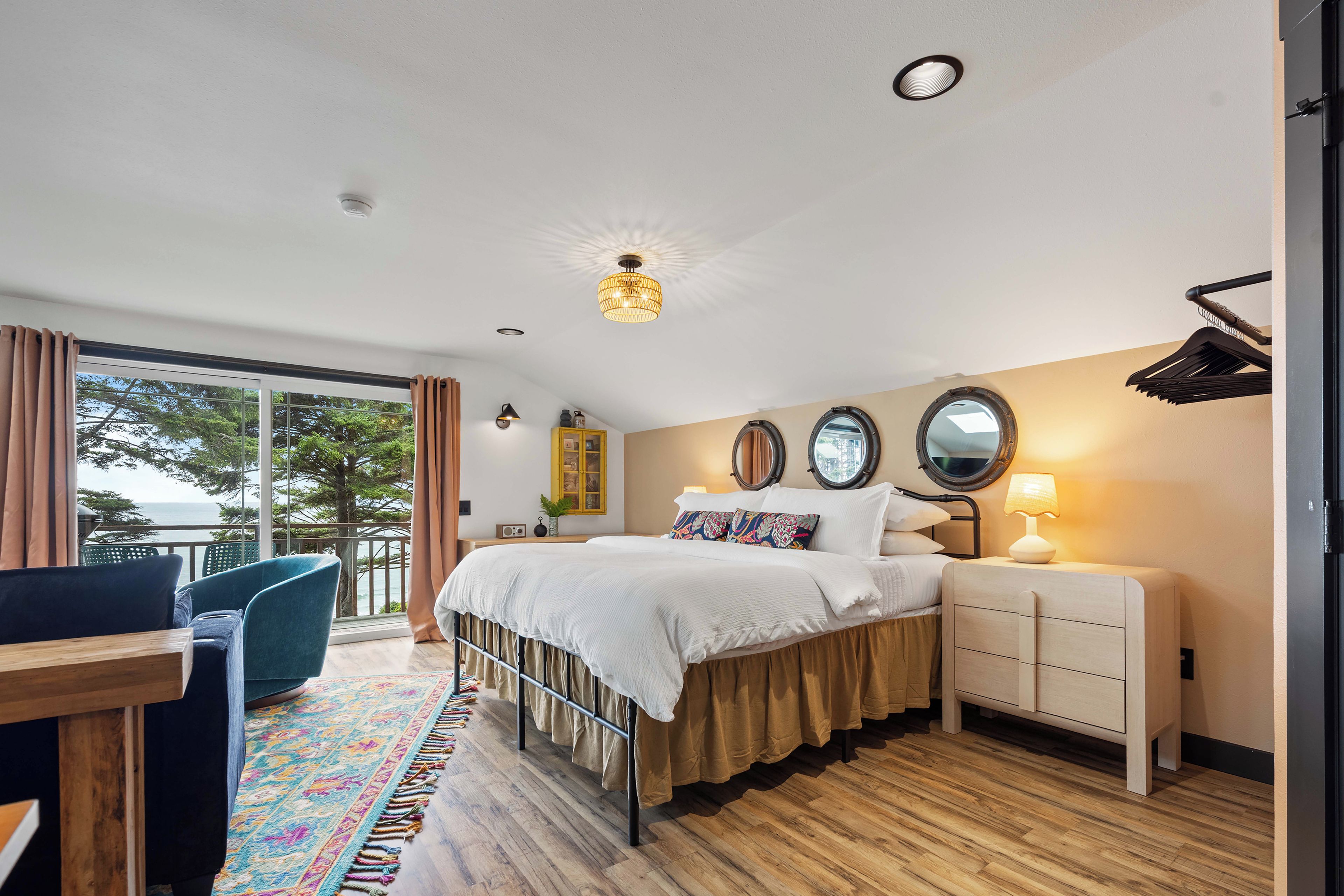 A bedroom with a bed, bedside table, lamp, and a view of the outdoors.