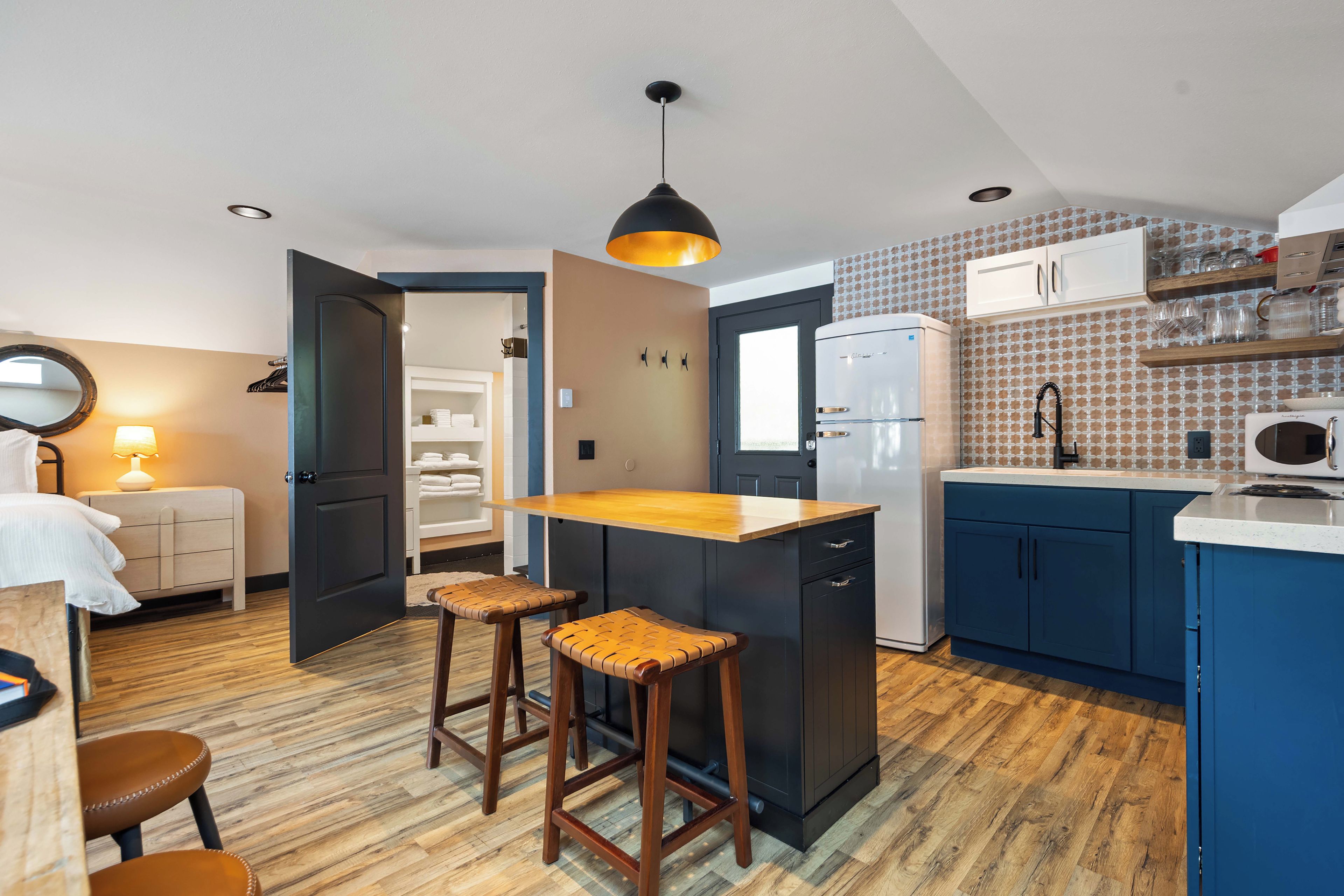 Una cocina compacta con una isla central, taburetes de bar, un refrigerador y un microondas.