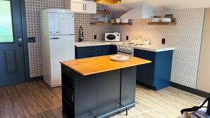 Cocina compacta con refrigerador, microondas, estufa y una isla de encimera de madera.