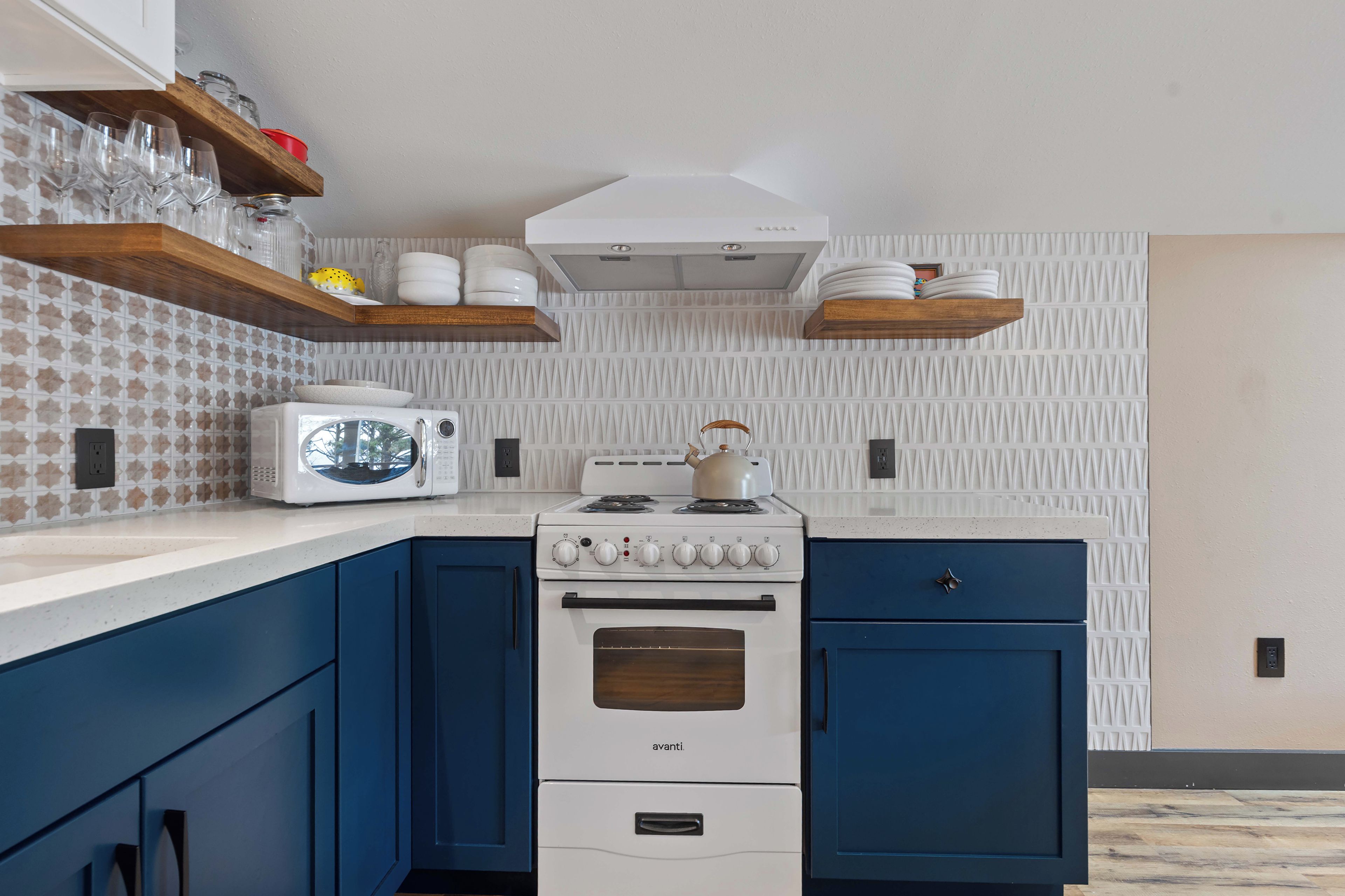Een keuken met een witte kookplaat, blauwe keukenkastjes en een magnetron op het aanrecht.