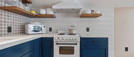 Een keuken met een witte kookplaat, blauwe keukenkastjes en een magnetron op het aanrecht.
