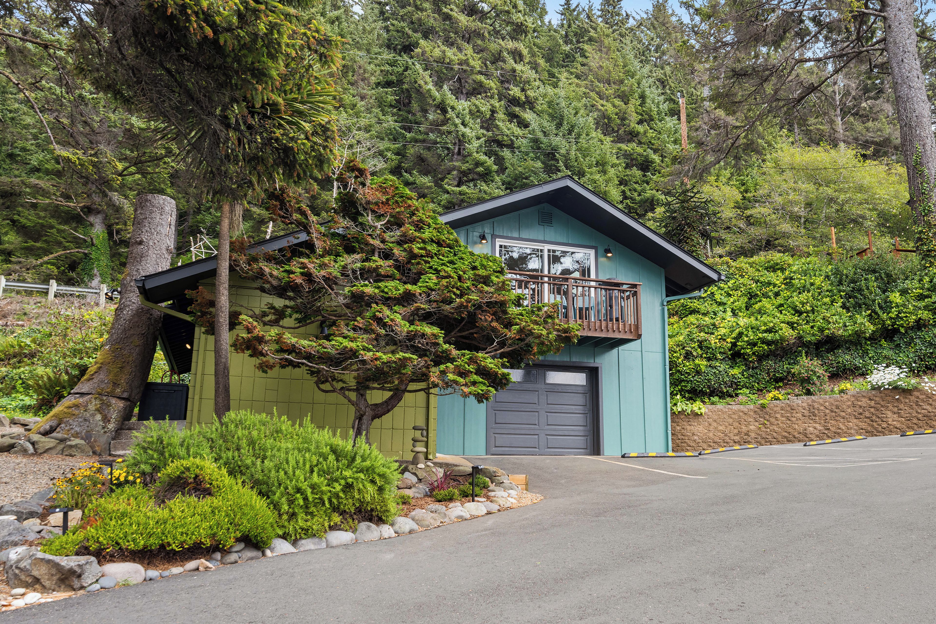 A small, single-story building with a balcony, surrounded by dense forest.
