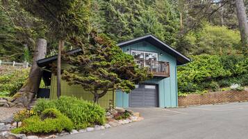 A small, single-story building with a balcony, surrounded by dense forest.