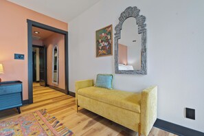 Quarto com sofá amarelo, tapete estampado, espelho e um quadro na parede.