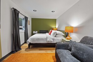 Quarto de hotel com cama, escrivaninha, cadeira, luminária e janela com cortinas.