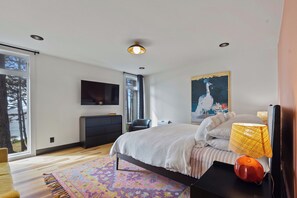 A modern bedroom with a bed, a desk, a chair, a TV, and a large window.