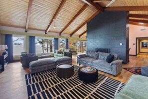 A spacious living room with a high ceiling, a fireplace, and a view of the outdoors.