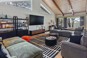 A modern living room with a flat-screen TV, a bookshelf, a sofa set, and a view of the outdoors.