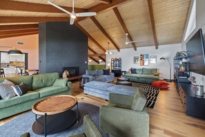 Uma sala de estar ampla com pé direito alto, vigas de madeira aparentes e lareira.