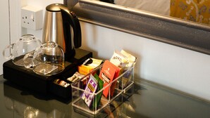 Une chambre d’hôtel comprenant un lit, une table de chevet avec une bouilloire, une cafetière en verre et un plateau avec divers articles.