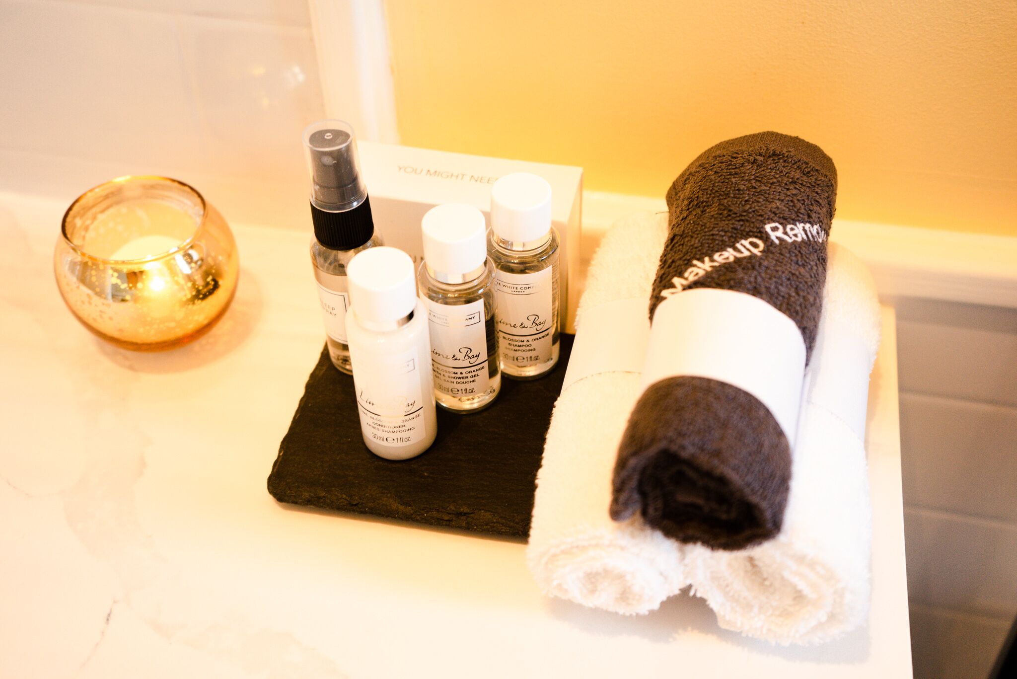 A bathroom with a towel, a candle, and various toiletries on a shelf.