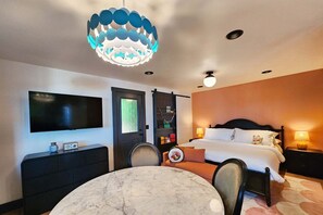 A hotel room with a bed, bedside table, lamp, TV, and a unique ceiling light fixture. - Ocean Front, The Fishwives' Cottage, Stairs to the Beach! (Yachats)