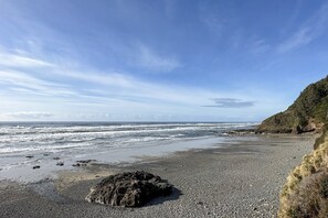 Une plage rocheuse avec des vagues, un ciel dégagé et une falaise boisée.
