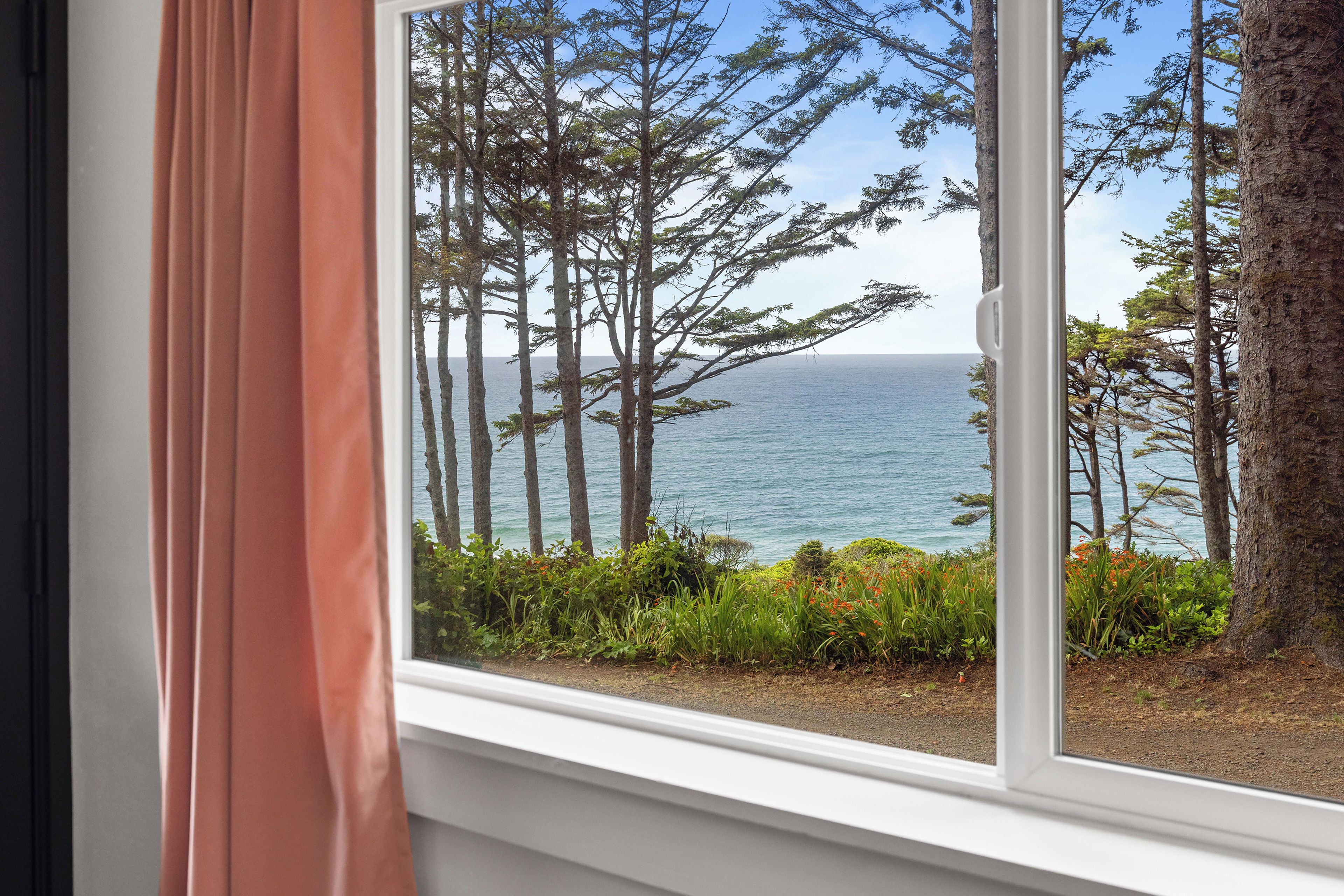 A window with a view of tall trees and a body of water.