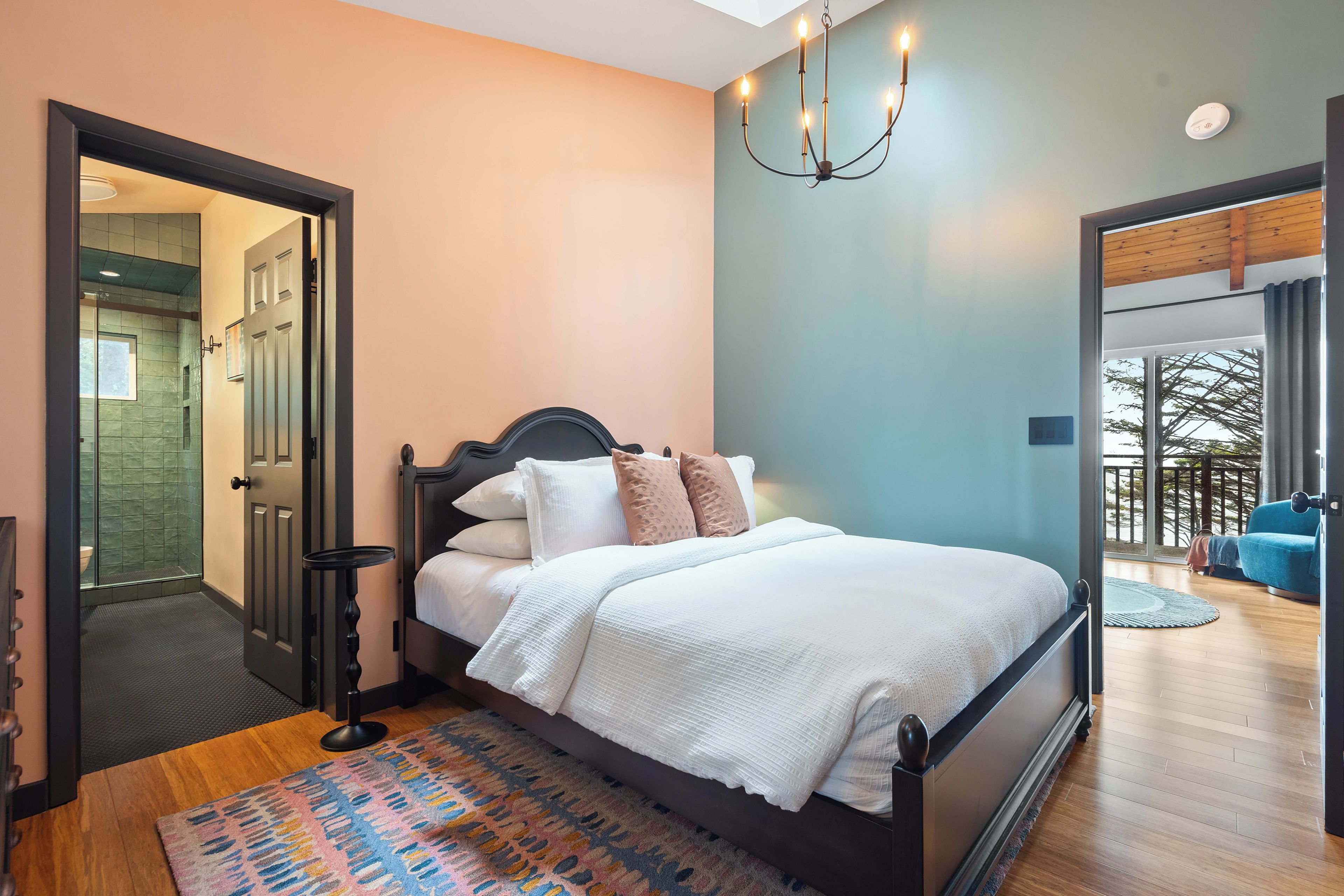 Une chambre à coucher avec un lit, un lustre, une salle de bain avec une porte en verre et une vue sur l’extérieur.